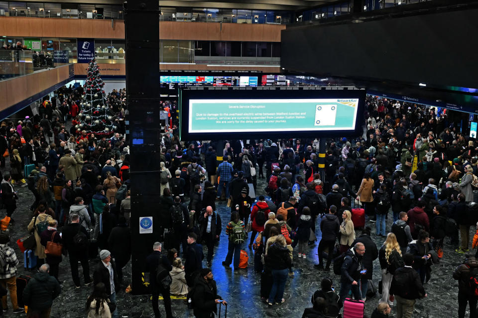 Rail travellers stand beneath an electronic information board displaying a message from Network Rail about damaged overhead wires leading to suspended services, at Euston Station in London on December 21, 2023, as services are disrupted due to damage caused by strong winds. A yellow weather warning for wind is in place until 9pm today, with forecasted gusts of 65mph to 70mph on high ground - and 45mph to 55mph elsewhere in the country. (Photo by JUSTIN TALLIS / AFP) (Photo by JUSTIN TALLIS/AFP via Getty Images)