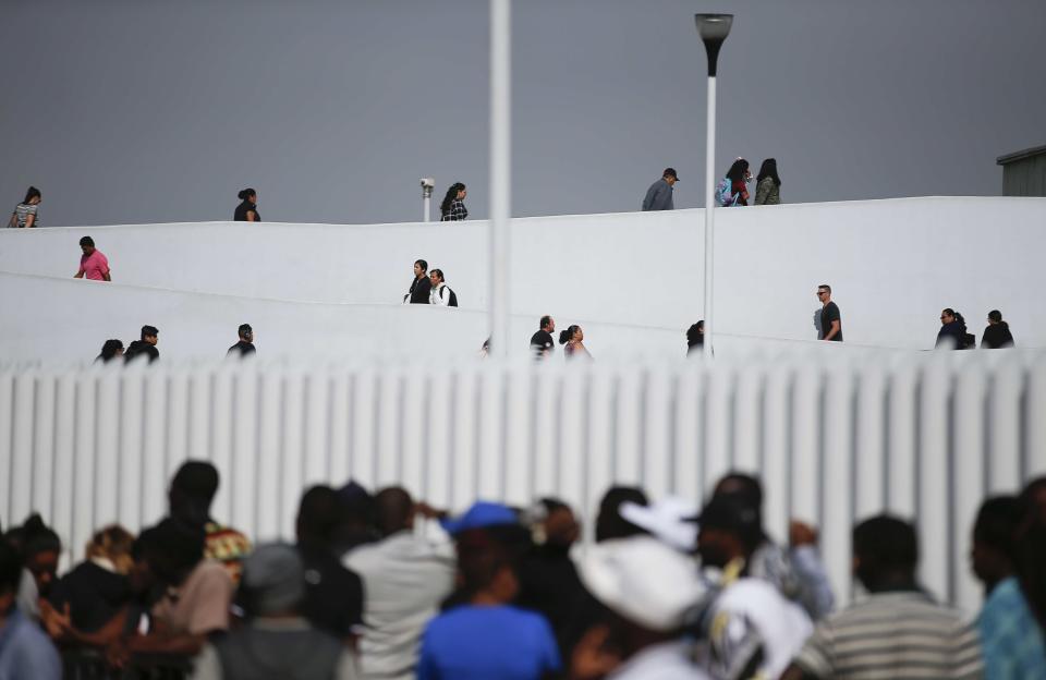 People use the legal border crossing into the United States, top, as migrants, below, wait to apply for asylum in the U.S., on the border in Tijuana, Mexico, Sunday, June 9, 2019. The mechanism that allows the U.S. to send migrants seeking asylum back to Mexico to await resolution of their process has been running in Tijuana since January. (AP Photo/Eduardo Verdugo)