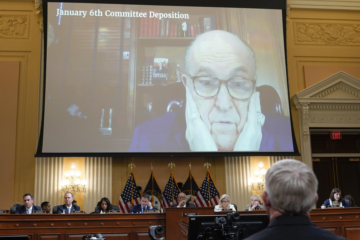 A video marked January 6th Committee Deposition shows Rudy Giuliani cupping his face in his hands above the panel.