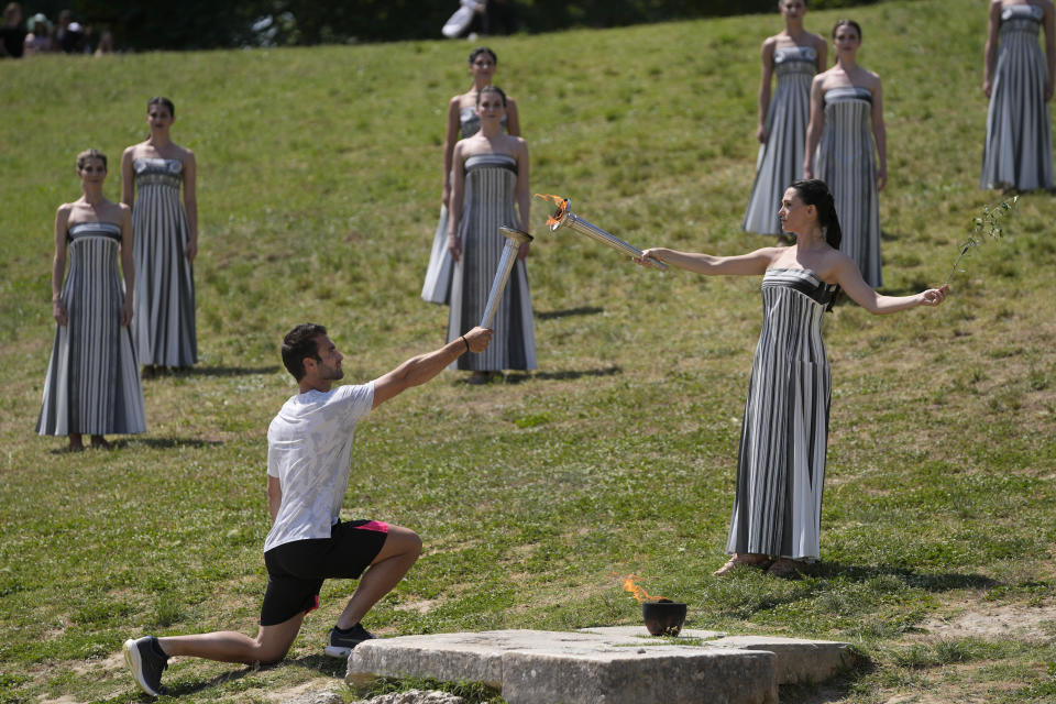 La actriz Mary Mina, quien realiza el papel de sacerdote le pasa la flama olímpica al primer relevo de la antoricha, el medallista olímpico griego Stefanos Douskos durante el último ensayo antes de la ceremonia del martes en Olimpia el lunes 15 de abril del 2024. (AP Foto/Thanassis Stavrakis)