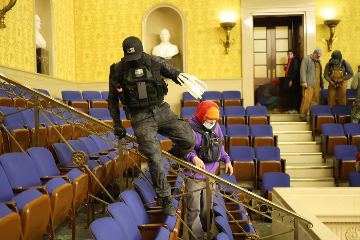 A man in camouflage swinging plastic hand restraints, identified by law enforcement as Eric Munchel, jumps among seats in the Capitol after it was stormed Jan. 6.