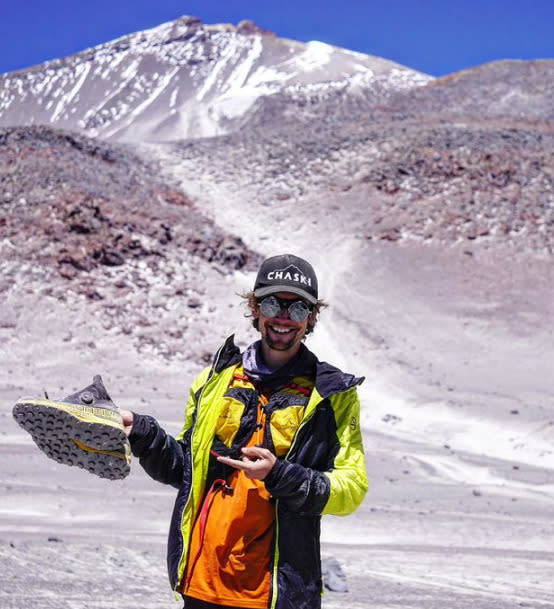 Andres with his shoes in the hand. capa nd sunglasses, in front of Ojos del Salado volcano.