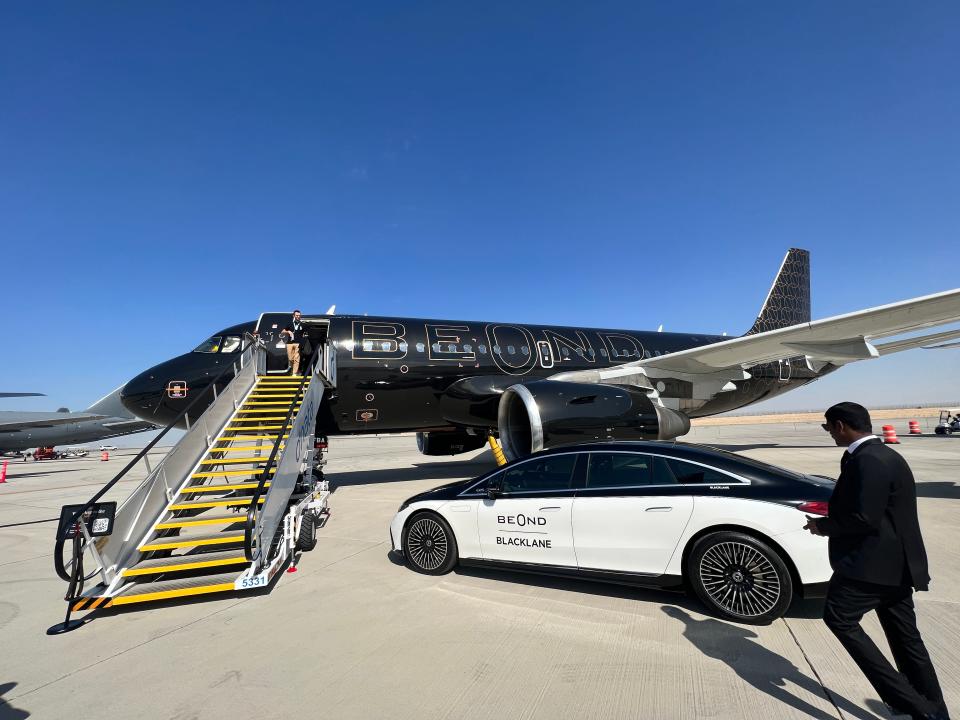 An Airbus A319 in Beond's black livery with gold accents is parked on the tarmac at the Dubai Air Show against a blue sky, a Beond-branded car is parked in front of the staircase
