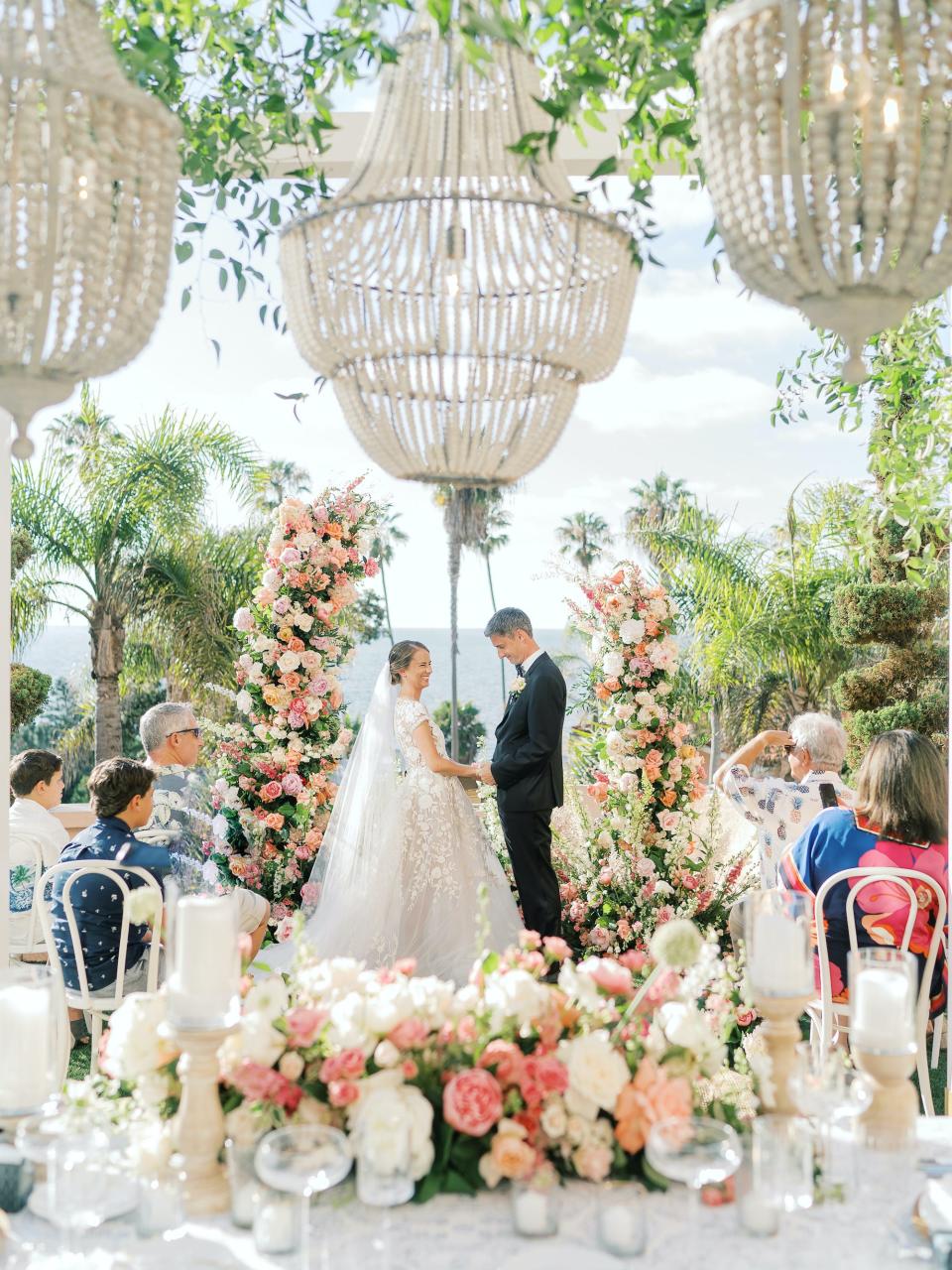 A bride and groom hold hands at their wedding altar that is surrounded by peach and white flowers.