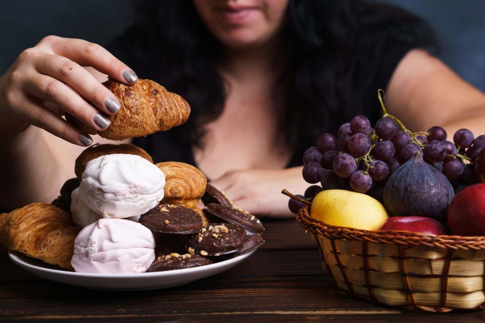 Sugar addiction, nutrition choices, conscious eating, overeating. Cropped portrait of overweight woman choosing between junk sweet food and fruits