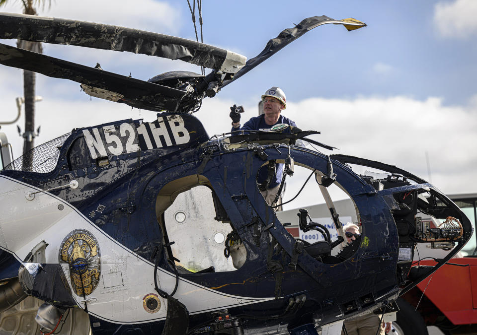 An investigator with the National Transportation Safety Board, NTSB, photographs the wreckage of a Huntington Beach helicopter in Newport Beach, Calif., Sunday, Feb. 20, 2022. Authorities were investigating the cause of a police helicopter crash along the Southern California coast that killed one officer and sent another to the hospital with critical injuries. The crashed killed Huntington Beach Officer Nicholas Vella, a 14-year veteran of the force. (Mindy Schauer/The Orange County Register via AP)