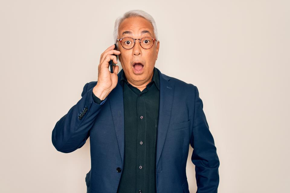 Middle age senior grey-haired business man wearing glasses talking on smartphone scared in shock with a surprise face, afraid and excited with fear expression