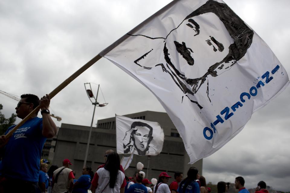 A worker of the National Telecommunications Company, CANTV, holds a banner with a line drawing of Venezuela's President Nicolas Maduro during a pro-government rally in Caracas, Venezuela, Tuesday, Feb. 25, 2014. The acronym INFOCENTRO running along the side banner represents a government program that provides internet services free of charge. (AP Photo/Rodrigo Abd)