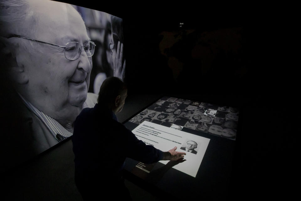 Jorge Tredler, 83, of Poland, who came to Brazil with his family in Feb. 1951 after taking refuge in Russia and other countries during the second World War, points to a photo of his father Szymon on an interactive table that tells the stories of thousands of people who took refuge in Brazil during the Holocaust, at the Holocaust Victims Memorial on its opening day to the public in Rio de Janeiro, Brazil, Thursday, Jan. 19, 2023. Another photo of his father is displayed at left. (AP Photo/Bruna Prado)