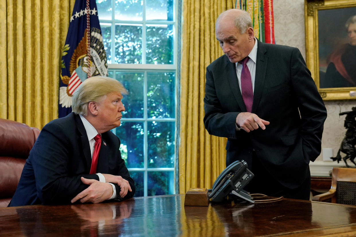 President Donald Trump, seated at his desk, looks bullish as his White House chief of staff, John Kelly, standing, leans in to make a point.