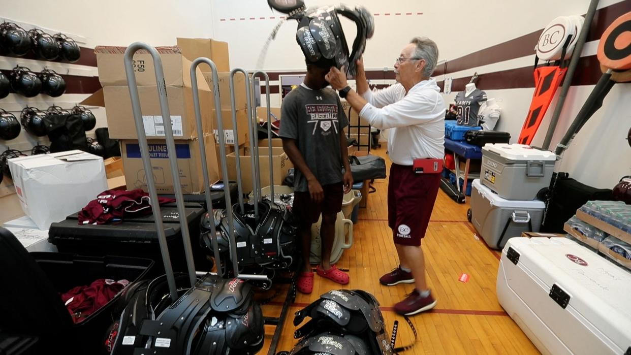 Long time Benedictine coach Charles Jung helps to fit a Cadet with new shoulder pads at the beginning of the football season.