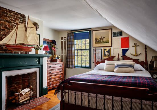 framed art and maps cover the walls of this nautical themed bedroom and the bed has a plaid spread and striped pillows