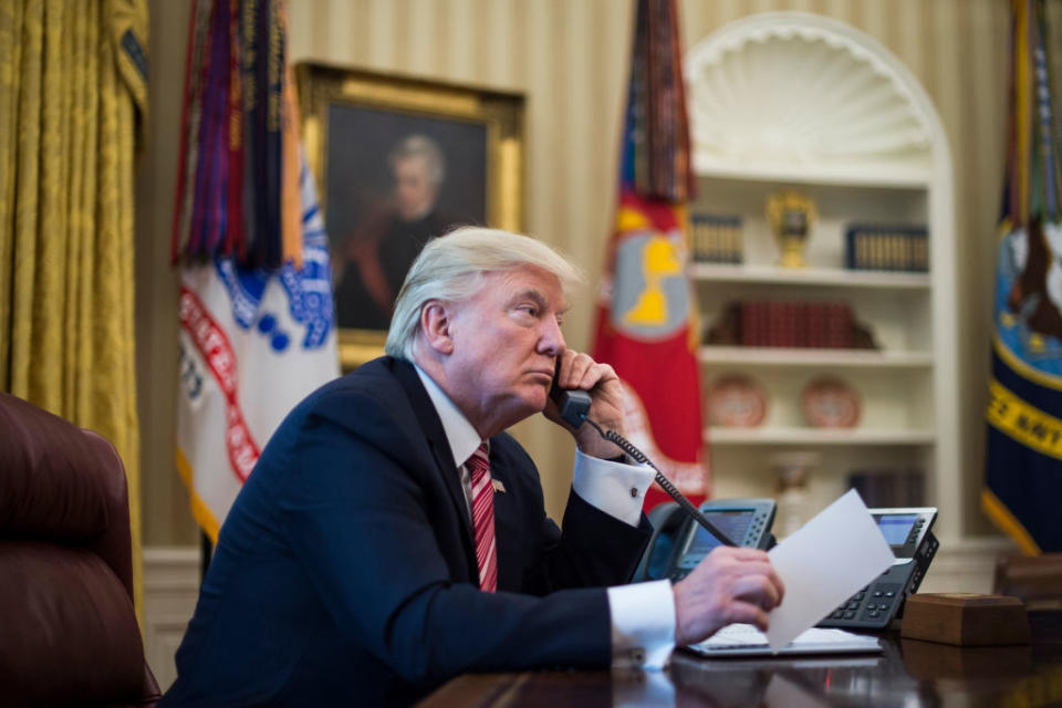 President Donald Trump speaks on the telephone while sitting in the Oval Office. 