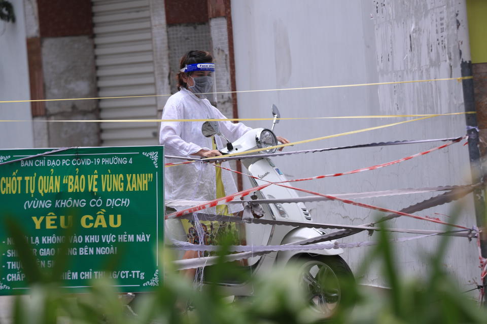 A woman stops her scooter as the alley is blocked with cordon tapes in Vung Tau, Vietnam, Monday, Sept. 13, 2021. The roadblocks and barricades make the streets of this southern Vietnamese city look like they did during the war that ended almost 50 years ago. But this time, the battle is being fought against the rampaging coronavirus.(AP Photo/Hau Dinh)