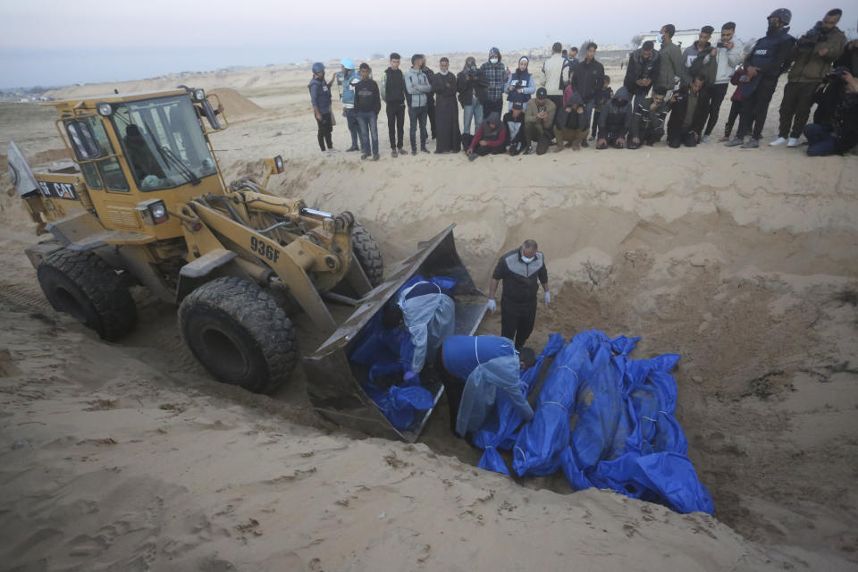 Bulldozer unloads the bodies of Palestinians killed in the north of the Gaza Strip and turned over by the Israeli military during a mass funeral in Rafah, Tuesday, Dec. 26, 2023. (AP Photo/Hatem Ali)