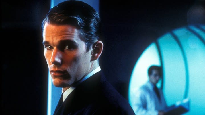 Ethan Hawke in a suit looking back, someone in a white lab coat in the distance behind him in a scene from Gattaca.