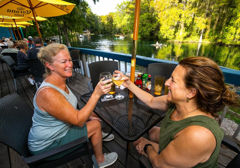 Longtime friends Jeri Littrell, left, and Karen Pause-Meeks, right, toast one another while enjoying a glass of wine on the Rainbow River at Swampy's in Dunnellon.