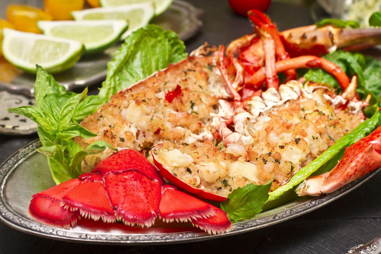 Closeup of roasted lobster on a silver plate with lettuce with a blurred background of limes and food