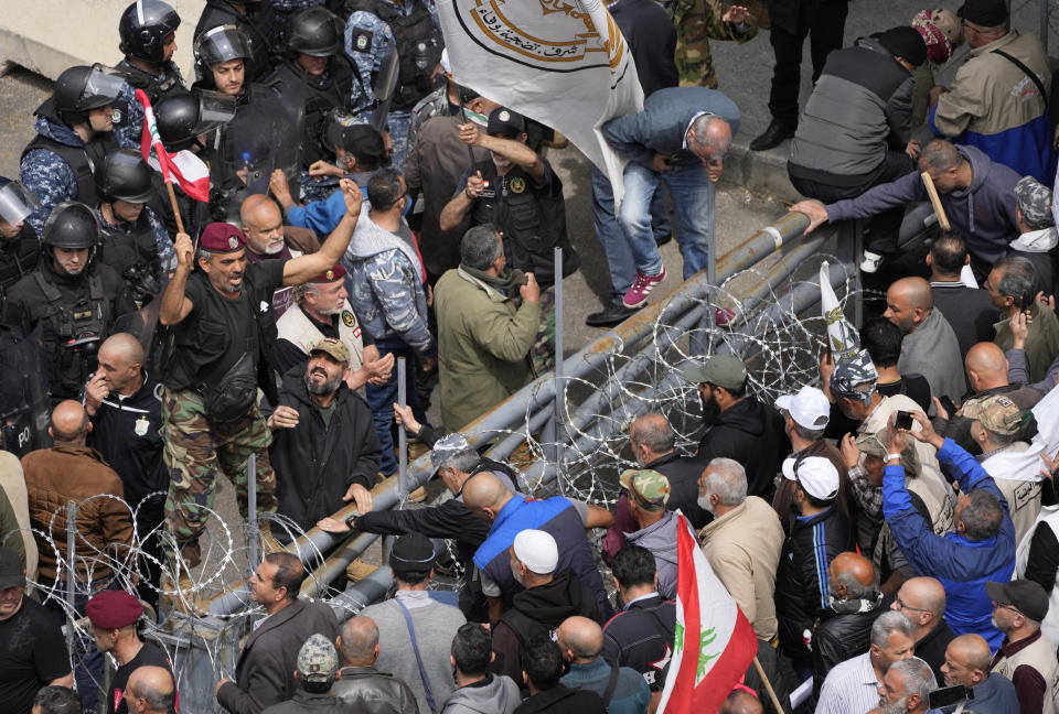 A retired army soldier, left top, calls other protesters to cross barriers and reach the government palace, in Beirut, Lebanon, Wednesday, March 22, 2023. Lebanese security forces fired tear gas to disperse hundreds of protesters who tried to break through the fence leading to the government headquarters in downtown Beirut Wednesday amid widespread anger over the harsh economic conditions in the country.(AP Photo/Hussein Malla)