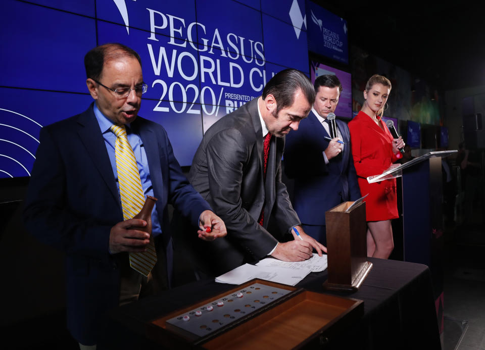 Stakes coordinator Eric Friedman, left, draws a number as assistant racing secretary Michael Costanzo, second from left, pulls out a horse's name during the draw for the Pegasus World Cup Horse Race, Wednesday, Jan. 22, 2020, in Hallandale Beach, Fla. At right are racing analysts Acacia Courtney and Jason Blewitt, second from right, The race will run Saturday, Jan. 25. (AP Photo/Wilfredo Lee)