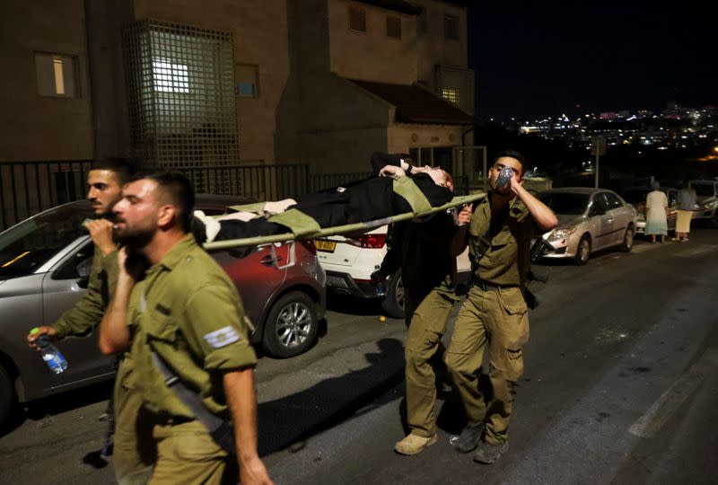 Members of the military carry injured people outside a synagogue in Givat Zeev