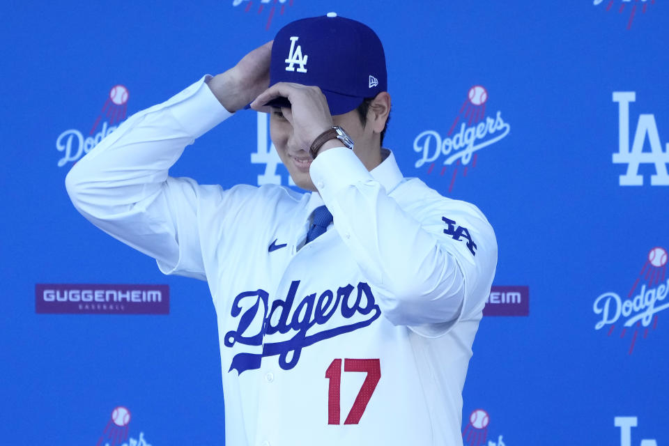 Los Angeles Dodgers' Shohei Ohtani puts on a baseball cap during a news conference at Dodger Stadium Thursday, Dec. 14, 2023, in Los Angeles. (AP Photo/Marcio Jose Sanchez)