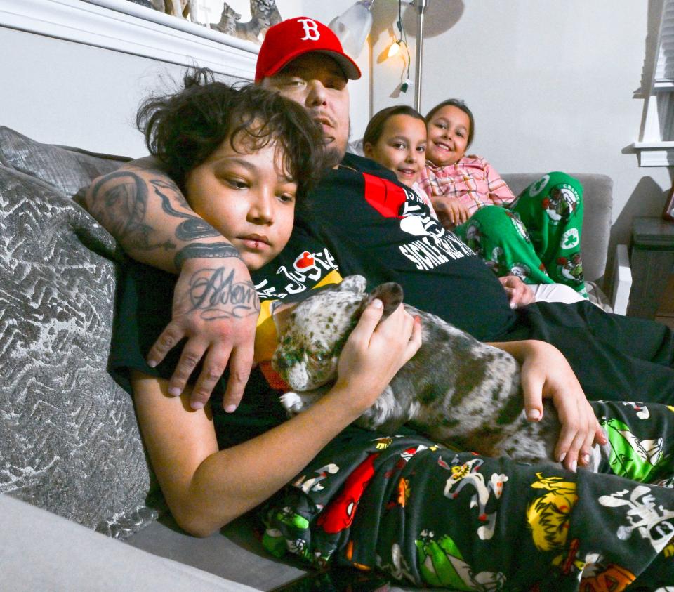 Aubrey "A.J." Wilsey of Mashpee sits with his son Jayden,13, who has sickle cell disease. Jayden holds his new French bulldog puppy, Floki. His 8-year-old sisters Isabelle (right) and Jasmine join them on their couch.