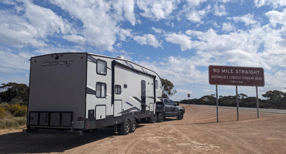 Large caravan imported from US parked by 'Australia's longest straight road' sign. 