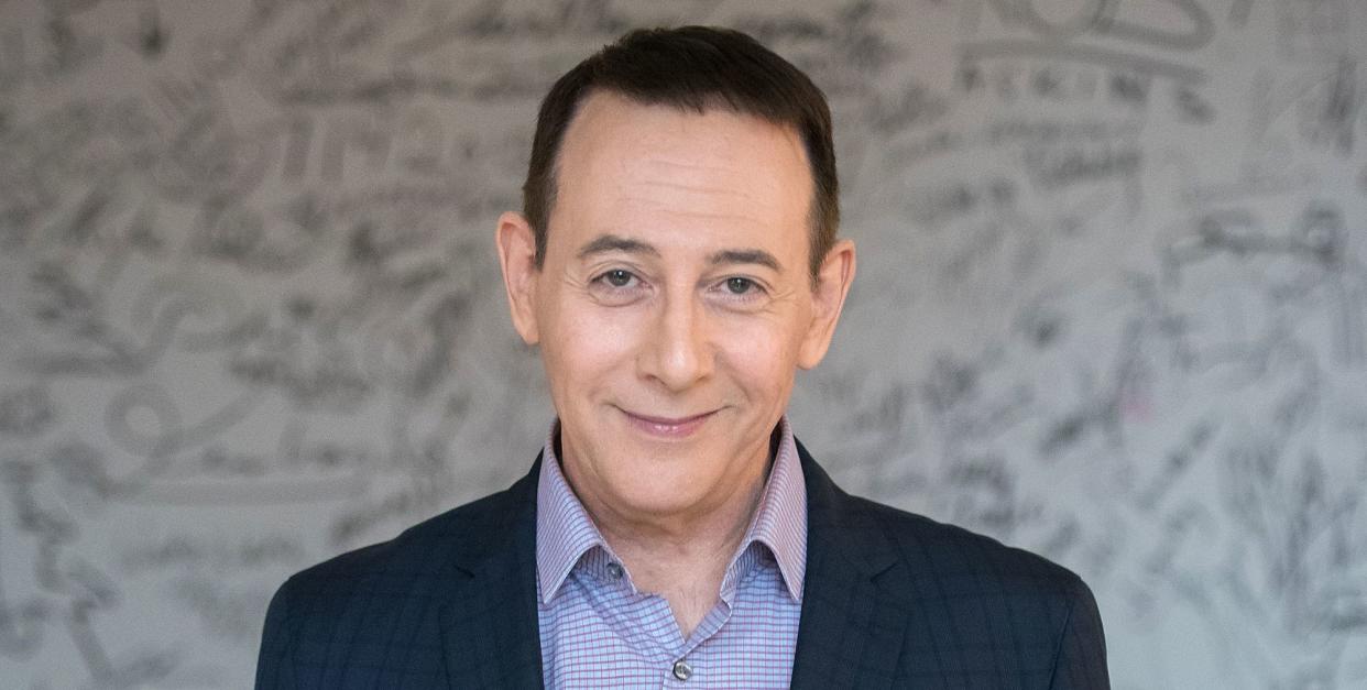 paul reubens wears a blue shirt and dark navy suit