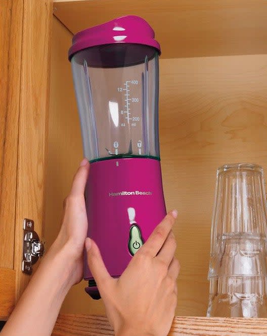 person placing a hamilton beach magenta blender in a kitchen cabinet