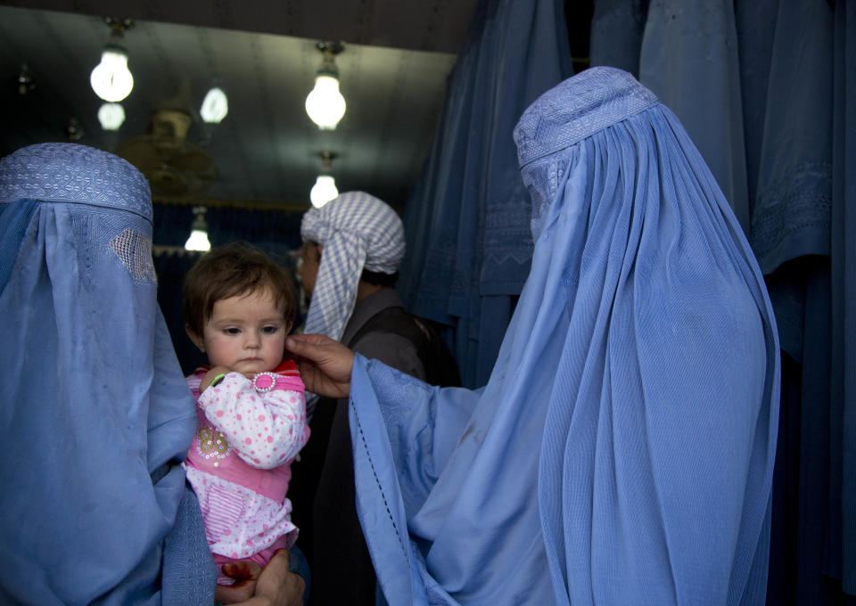 In this Thursday, April 11, 2013 photo. an Afghan woman comforts the child of her friend as both wait to get in line to try on a new burqa in a shop in the old town of Kabul, Afghanistan. Despite advances in women’s rights, Afghanistan remains a deeply conservative country and most women continue to wear the Burqa. But tradesmen say times are changing in Kabul at least, with demand for burqas declining as young women going to school and taking office jobs refuse to wear the cumbersome garments. (AP Photo/Anja Niedringhaus)