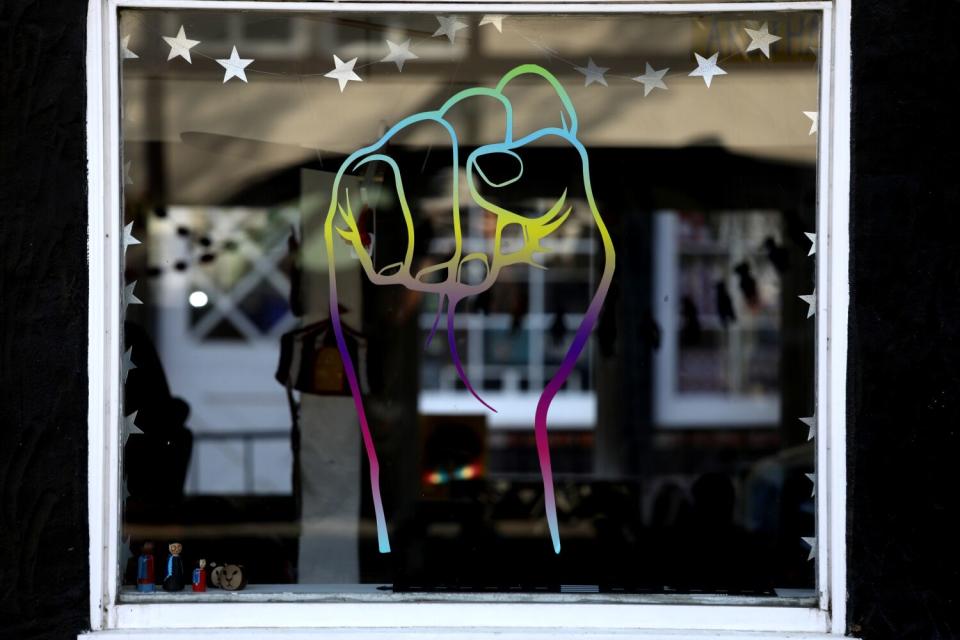 A stencil in a store window of a raised fist in rainbow colors.