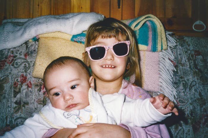 Two children, one with sunglasses, sitting together on a couch