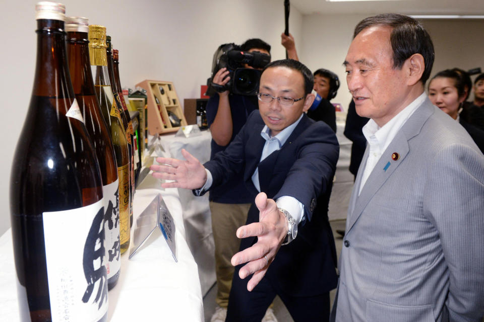 Then Chief Cabinet Secretary Yoshihide Suga, right, receives a briefing on hometown tax donation in Miyakonojo city, Miyazaki prefecture, southern Japan on June 15, 2016. Japan's Parliament elected Suga as prime minister Wednesday, Sept. 16, 2020, replacing long-serving leader Shinzo Abe with his right-hand man. Suga has stressed his background as a farmer's son and a self-made politician in promising to serve the interests of ordinary people and rural communities. (Kyodo News via AP)