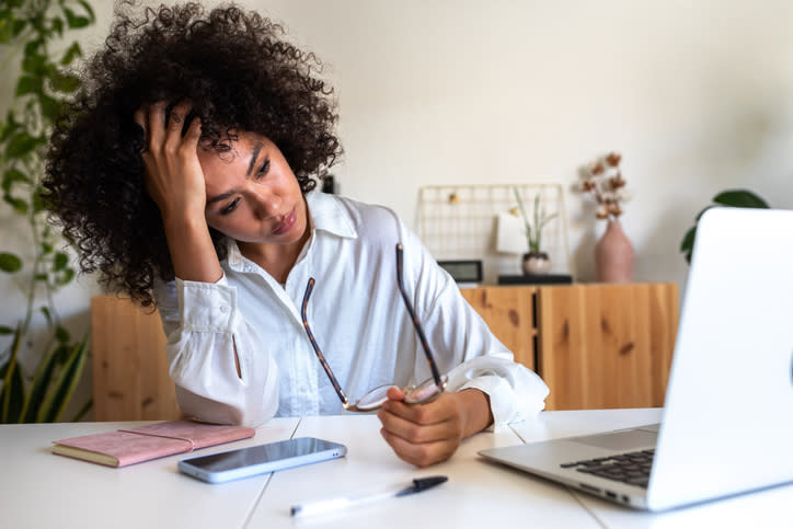 Person at a desk looks troubled with hand on forehead, near laptop and phone, possibly stressed or thinking deeply