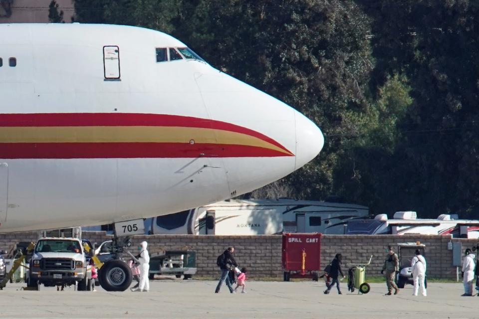 Women and children walks past personnel in protective clothing after arriving on an aircraft, chartered by the U.S. State Department to evacuate government employees and other Americans from the novel coronavirus threat in the Chinese city of Wuhan, at March Air Reserve Base in Riverside County, California, U.S., January 29, 2020. REUTERS/Mike Blake