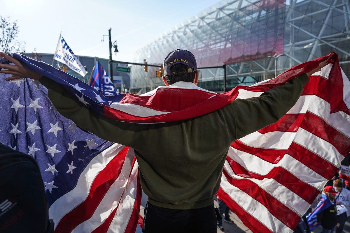 Michael Foy of Wixom, Michigan, holds his flag open while standing above the crowd gathered for a rally in support of President Trump outside of the TCF Center in Detroit on Friday, Nov 6, 2020 where the absentee ballot count for the city of Detroit took place.