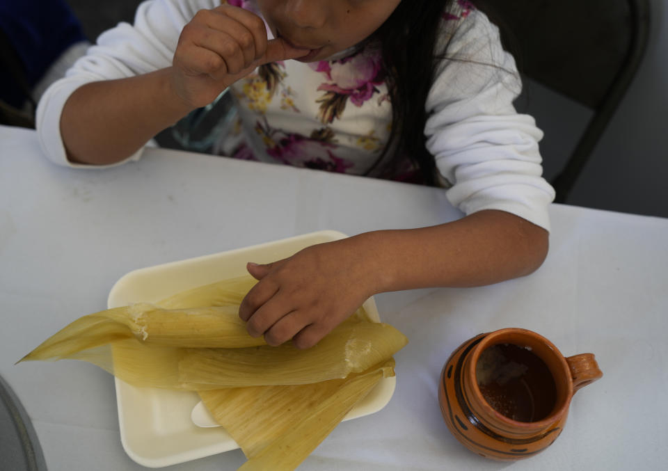 A girl enjoys a tamal during the opening of the tamales fair in the Ixtapalapa neighborhood of Mexico City, Friday, Jan. 27, 2023. Tamales date to pre-Hispanic times when Olmecs, Mexicas and Mayas prepared them for religious rituals, offerings and even placed them in tombs. (AP Photo/Fernando Llano)