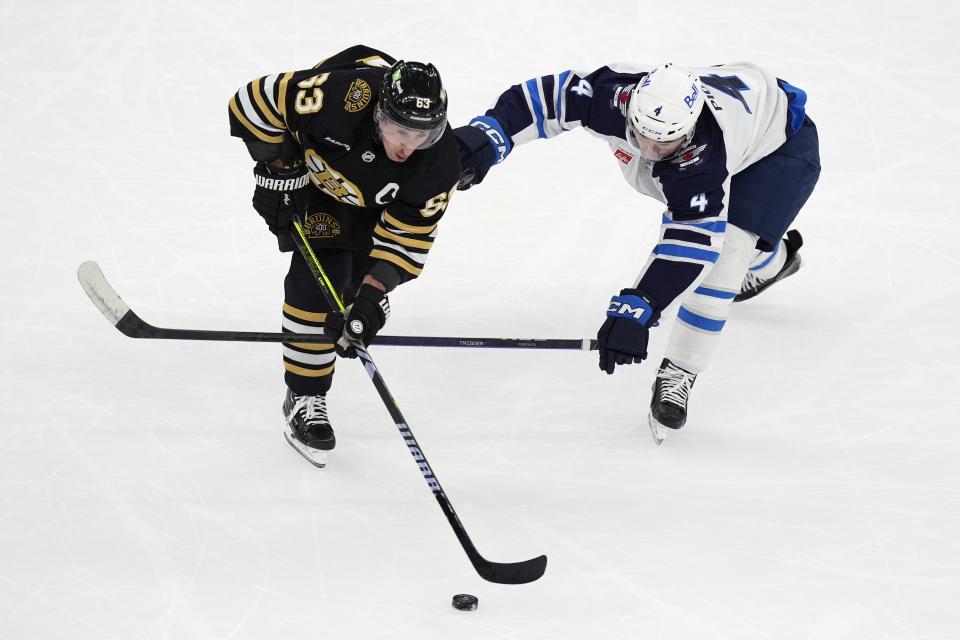 Winnipeg Jets' Neal Pionk (4) and Boston Bruins' Brad Marchand (63) battle for the puck during the first period of an NHL hockey game, Monday, Jan. 22, 2024, in Boston. (AP Photo/Michael Dwyer)