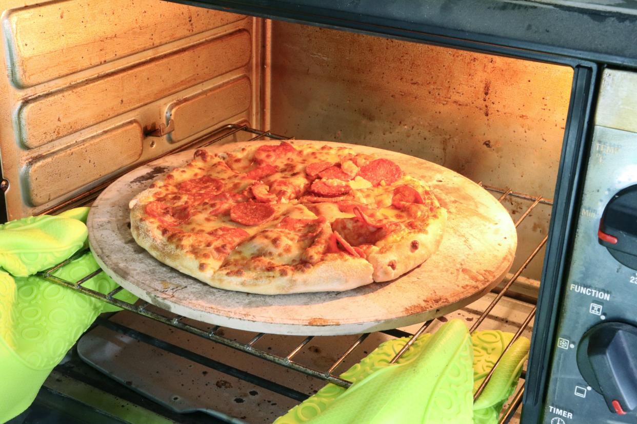 Stock photo showing close-up view of baked, homemade pepperoni pizza recipe with freshly made dough, tomato sauce, mozzarella cheese and pepperoni slice topping, cooked on pizza stone, for a crispy base, in a hot oven.