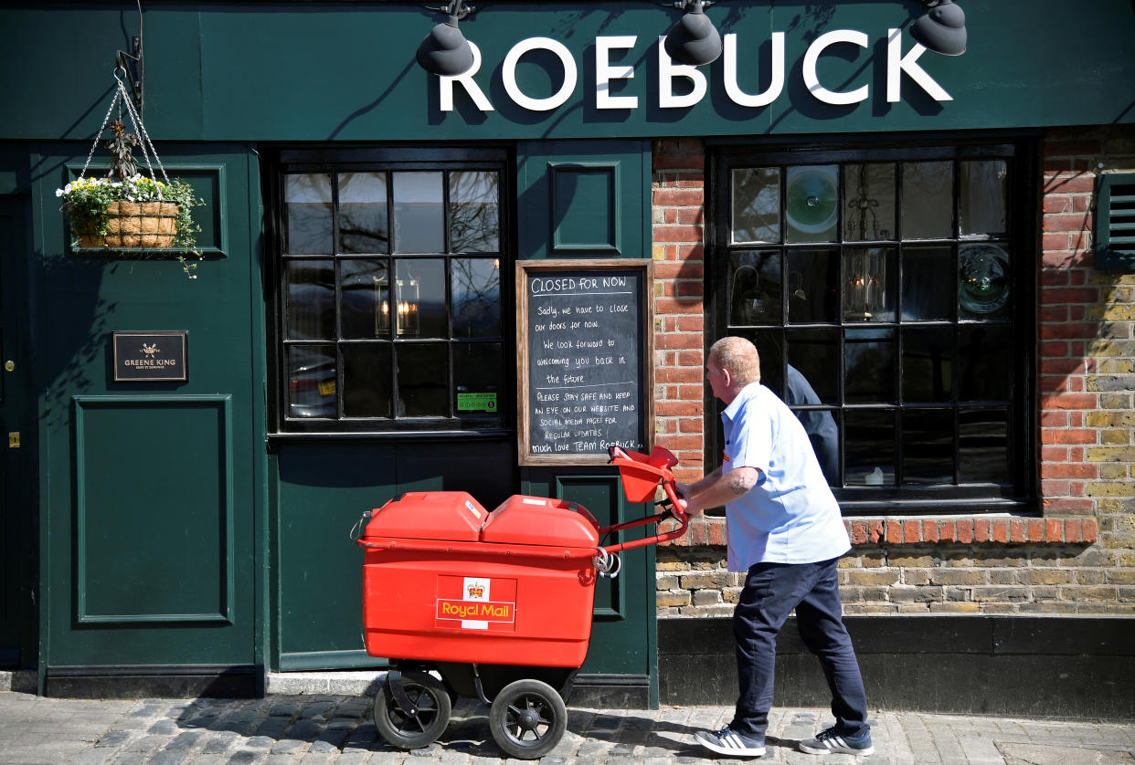 A Royal Mail delivery man looks at a "Closed" sign on a pub as he does his rounds, as the spread of the coronavirus disease (COVID-19) continues, in Richmond, London, Britain, March 24, 2020. REUTERS//Toby Melville