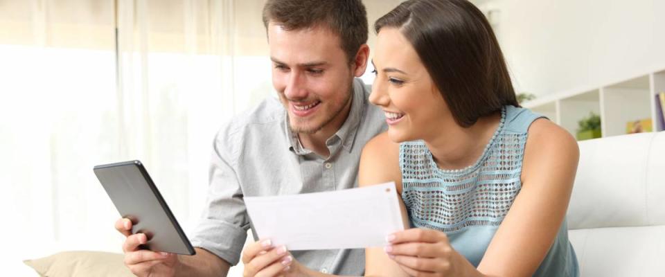 Happy couple checking bank account on line in a tablet sitting on a couch in the living room at home