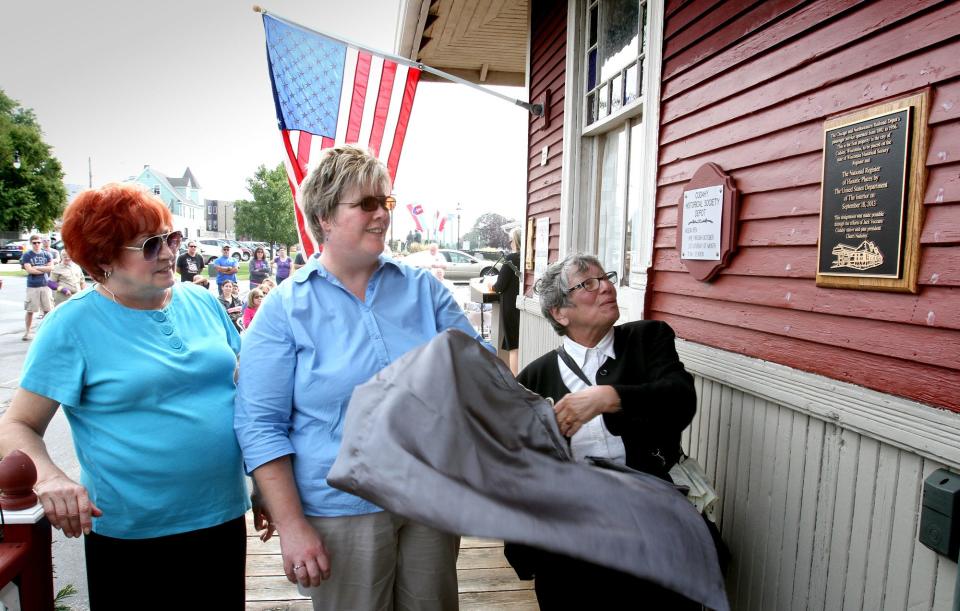 Charlene Pelfier (left), Jane Czarnezki and Ruth Raczak unveil a plaque that designates the Cudahy Train Depot's listing on the Wisconsin and National Registry of Historic Places during a dedication ceremony. The Chicago & Northwestern Depot served the community with passenger service from 1892 to 1956.