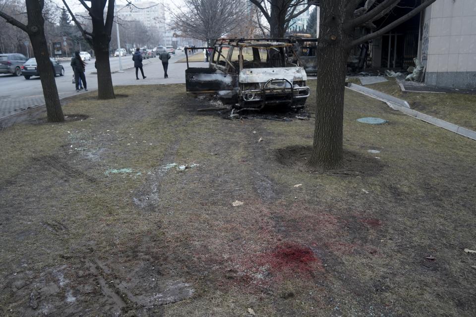 People walk past a bus, which was burned during clashes in Almaty, Kazakhstan, Tuesday, Jan. 11, 2022. Life in Almaty, which was affected with the violence the most during protests, started returning to normal this week, with public transport resuming operation and malls reopening. (Vladimir Tretyakov/NUR.KZ via AP)