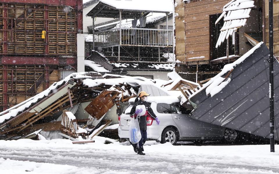 Person walks in front of fallen buildings in the earthquake-hit Anamizu, Ishikawa prefecture, Monday, Jan. 8, 2024. Thousands of people made homeless overnight are living in weariness and uncertainty on the western coast of Japan a week after powerful earthquakes hit the region. (Kyodo News via AP)