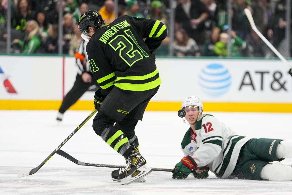 Minnesota Wild left wing Matt Boldy (12) eyes the puck while falling to the ice as Dallas Stars left wing Jason Robertson (21) competes for the puck during the first period of an NHL hockey game, Wednesday, Jan. 10, 2024, in Dallas. (AP Photo/Julio Cortez)