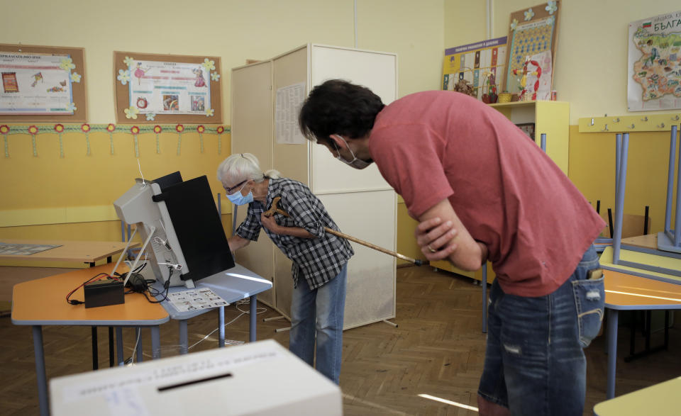 An elderly Bulgarian woman is assisted by an election commission member during her vote at a polling station in Sofia, Sunday, July 11, 2021. Bulgarians are voting in a snap poll on Sunday after a previous election in April produced a fragmented parliament that failed to form a viable coalition government. (AP Photo/Valentina Petrova)