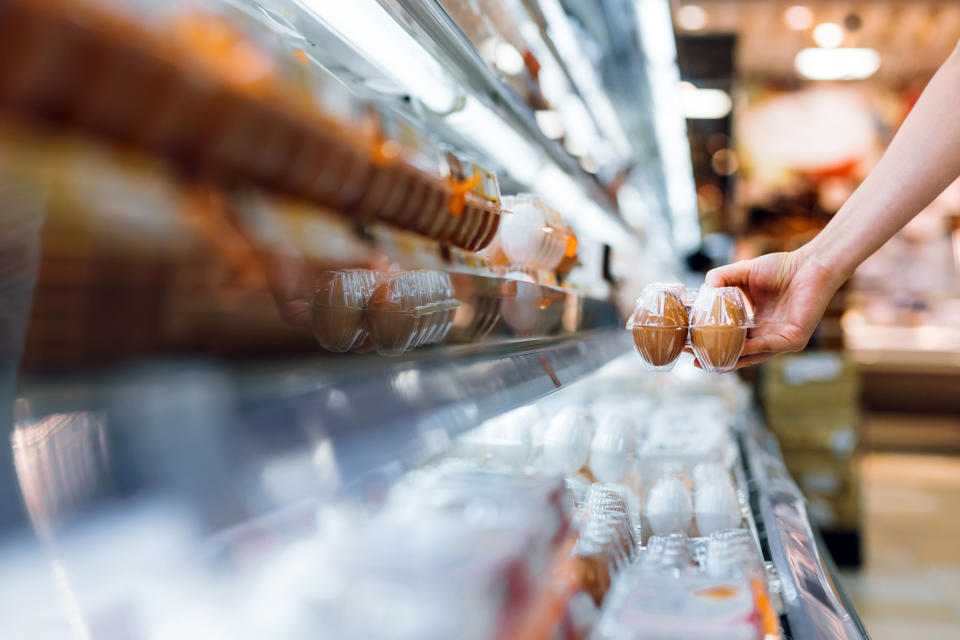 Close up of young woman grocery shopping in supermarket. She is holding a box of fresh organic free range eggs in front of refrigerated section. Healthy eating lifestyle