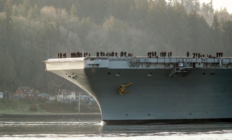 Sailors stand on the bow of the USS Theodore Roosevelt as it passes Bachmann Park in Bremerton, Wash. after leaving Puget Sound Naval Shipyard on Friday, March 17, 2023.