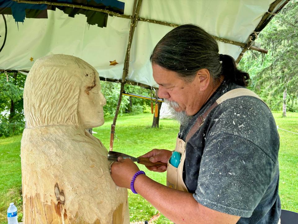 Wood sculptor Gene Delcourt carves the figure of an Indigenous woman from basswood at San Damiano Park in Monona on July 20. Delcourt, a former student of renowned Ho-Chunk artist Harry Whitehorse, is hosting a first-of-its-kind wood sculpture festival to honor his mentor.